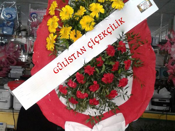 Sarı ve kırmızı çiçeklerden iki katlı ayaklı çelenk, dükkânın önünde