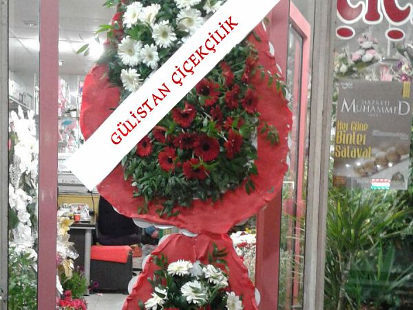 Dükkân önünde bekleyen, kırmızı gül ve beyaz çiçekli iki katlı çelenk