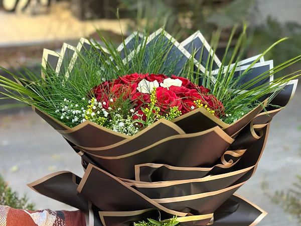 Siyah ve altın şeritli ambalaja sarılmış kırmızı gül buketi, elde tutuluyor