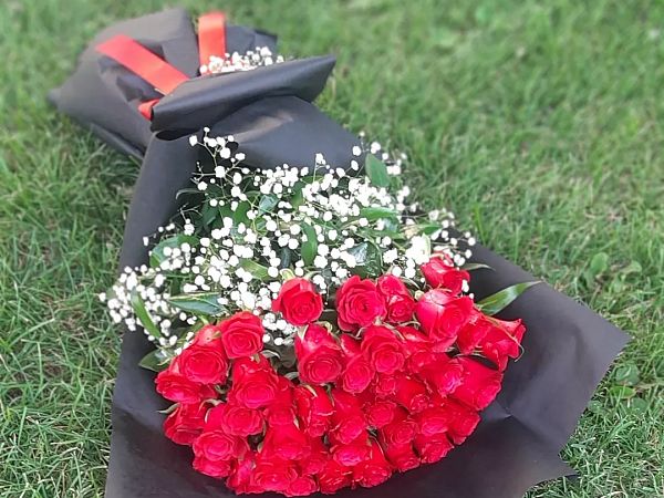 Kalp biçiminde dizilmiş kırmızı güller, siyah ambalaj üzerinde çimenlikte